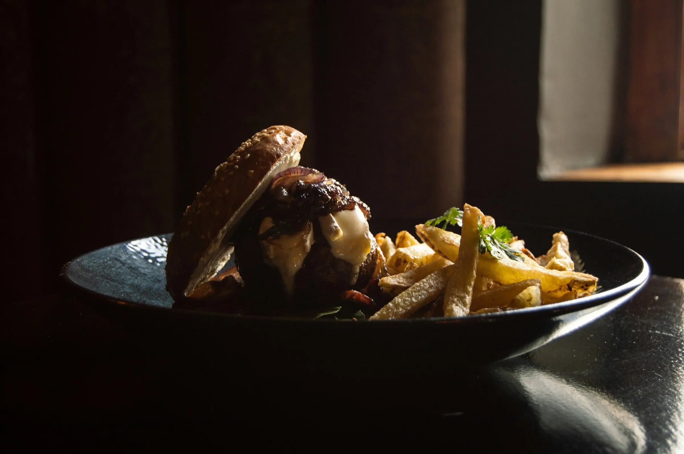 A burger and fries on a dark plate in warm window light